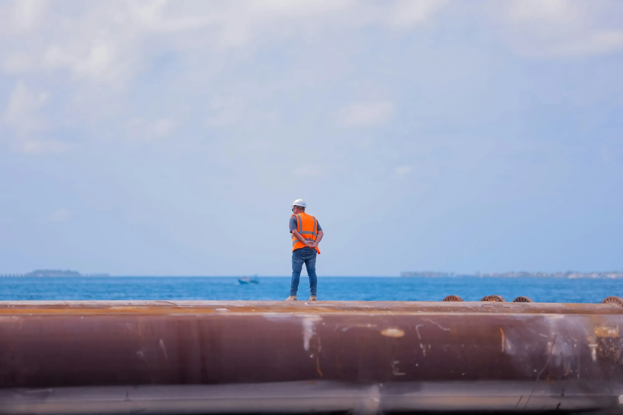 Arbeiter mit Schutzhelm und Warnweste auf einer großen Pipeline am Meer