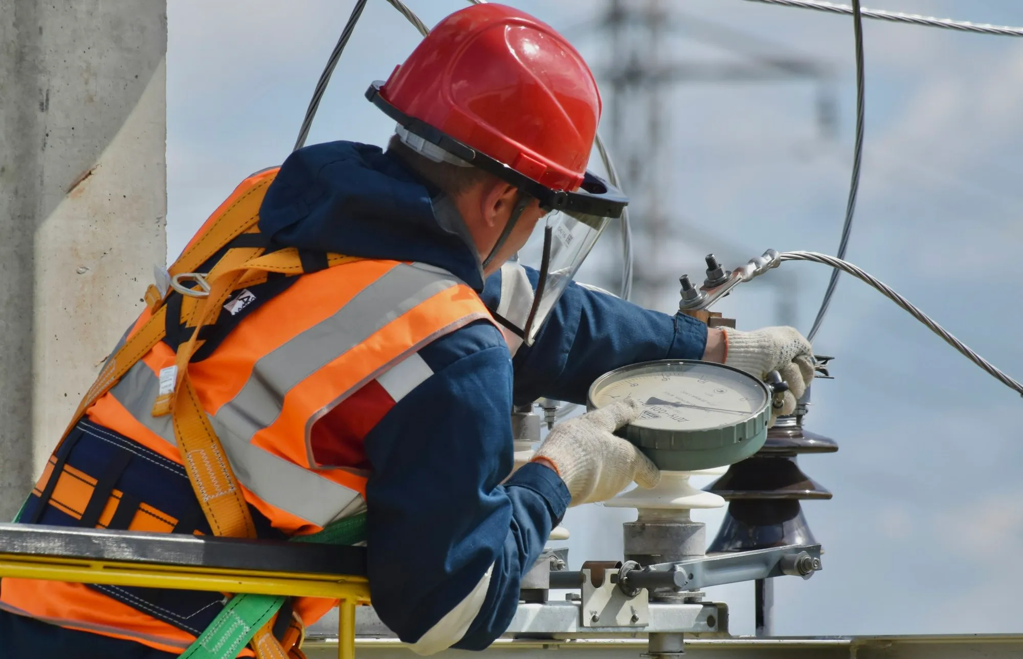 Technician in a hard hat and face shield reading a gauge on plant equipment
